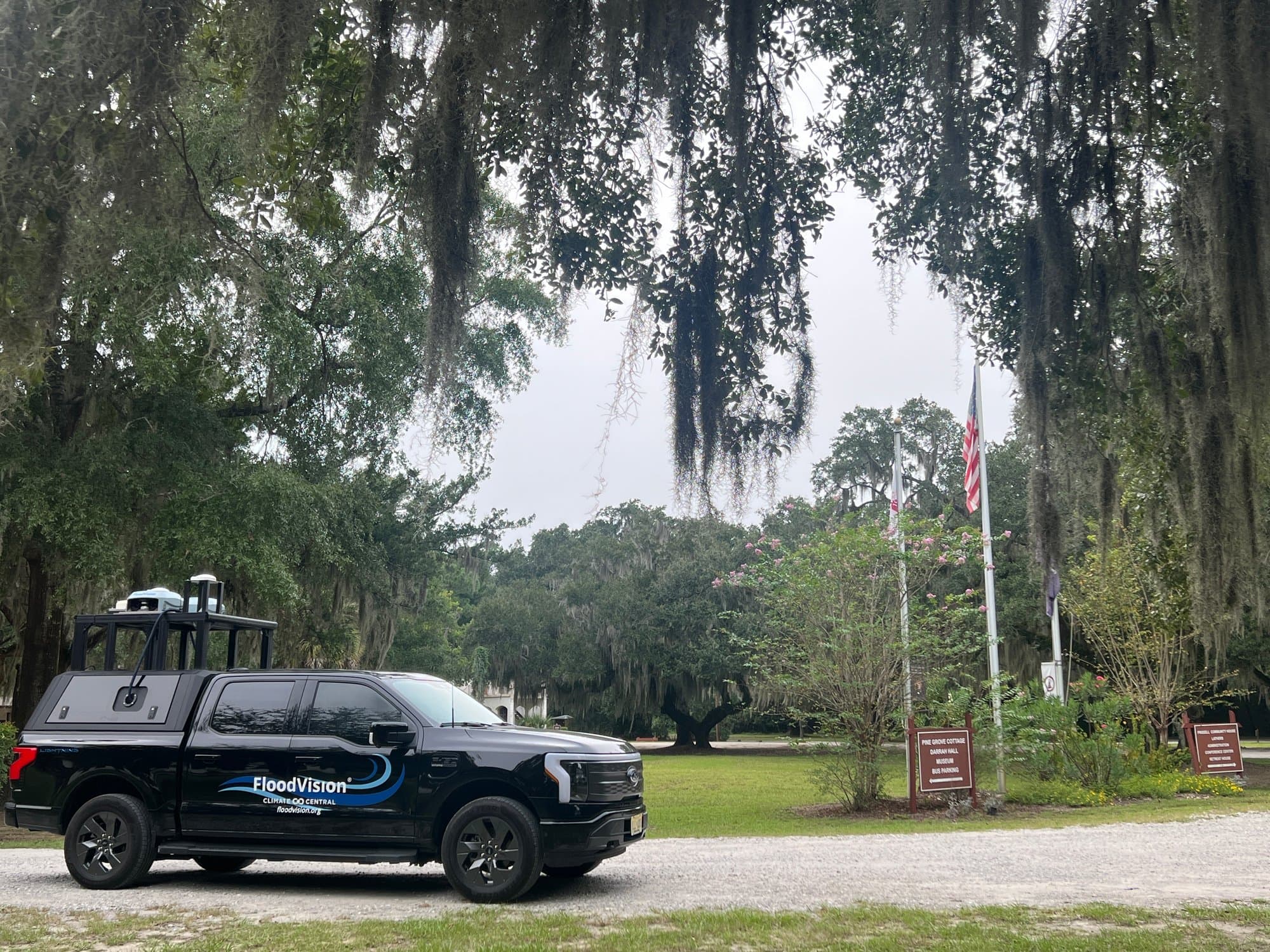 Black FloodVision survey truck with roof-mounted sensors on a tree-lined street
